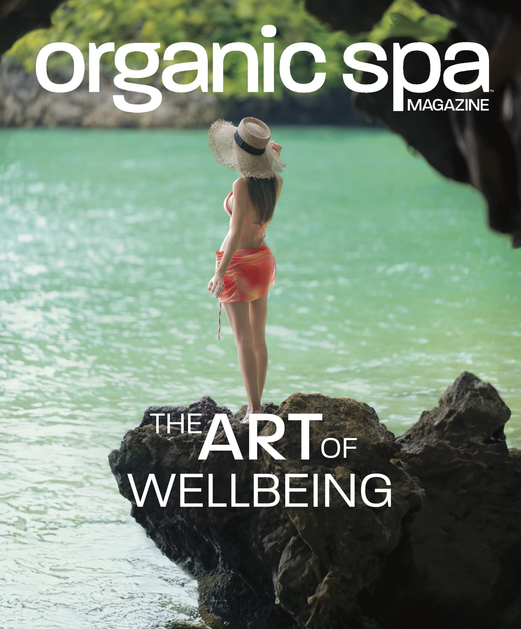 Woman in a hat and shorts standing on rocks over green water with 'Organic Spa Magazine' text.