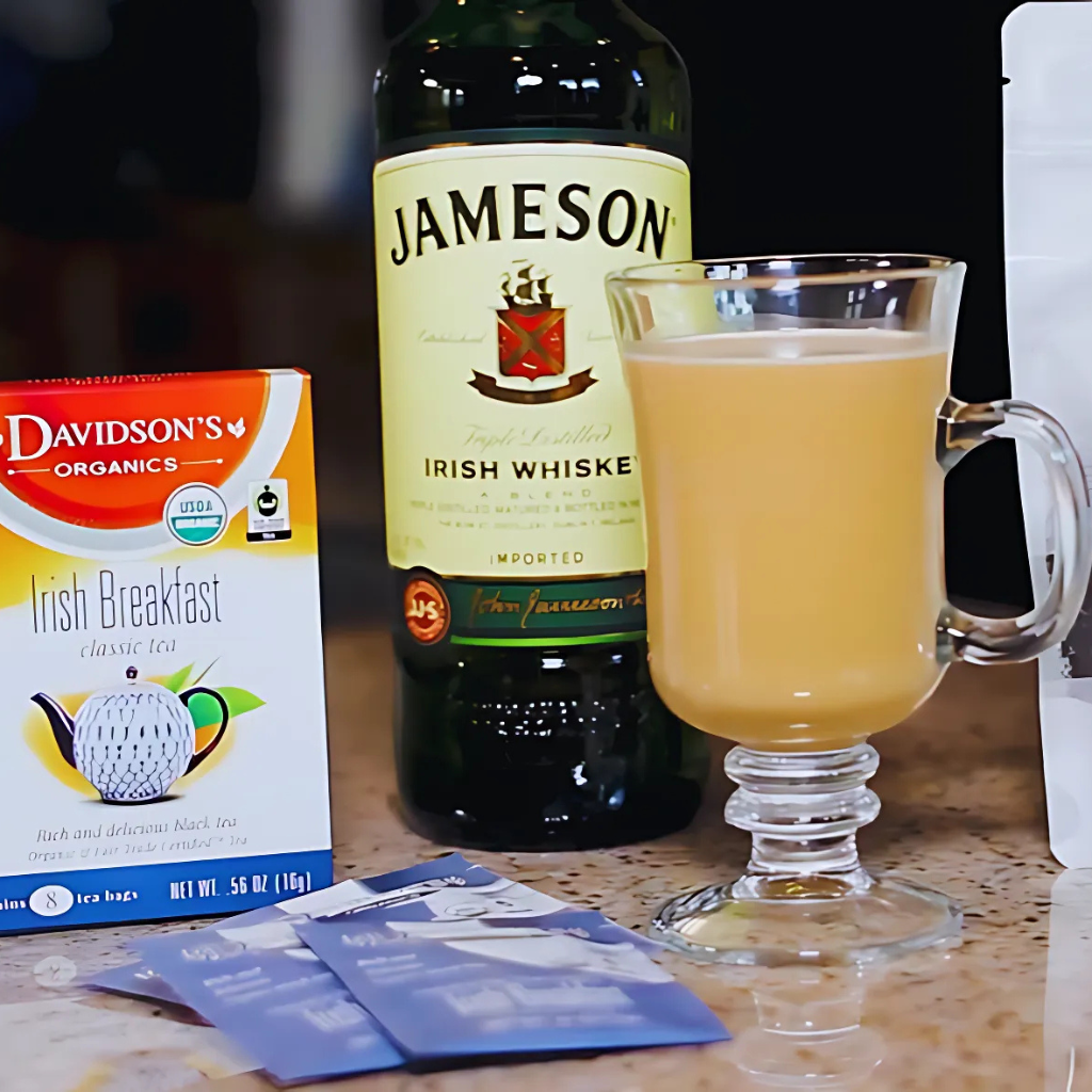Bottle of Jameson Irish Whiskey, glass with a drink, and box of Davidson's Irish Breakfast tea on a table.
