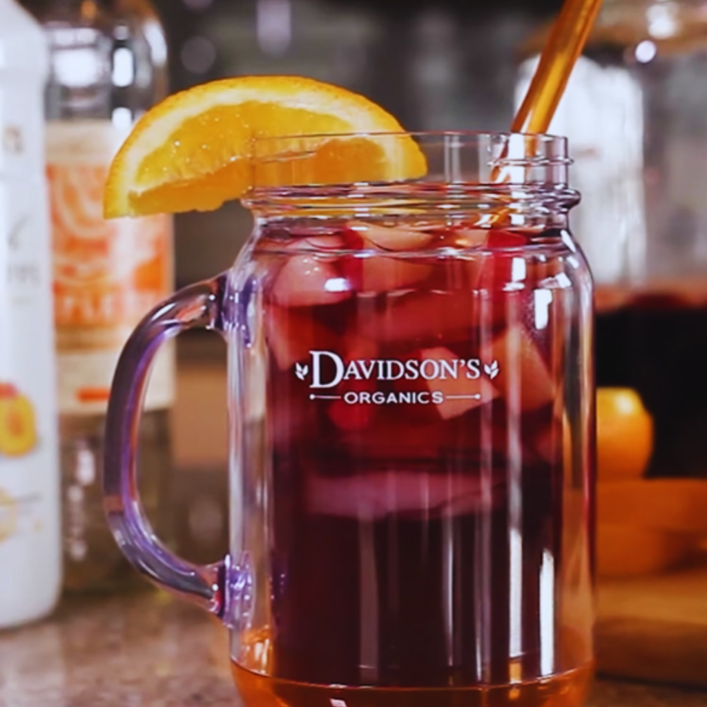 Glass mug with red liquid, orange slice, and straw on a blurred background