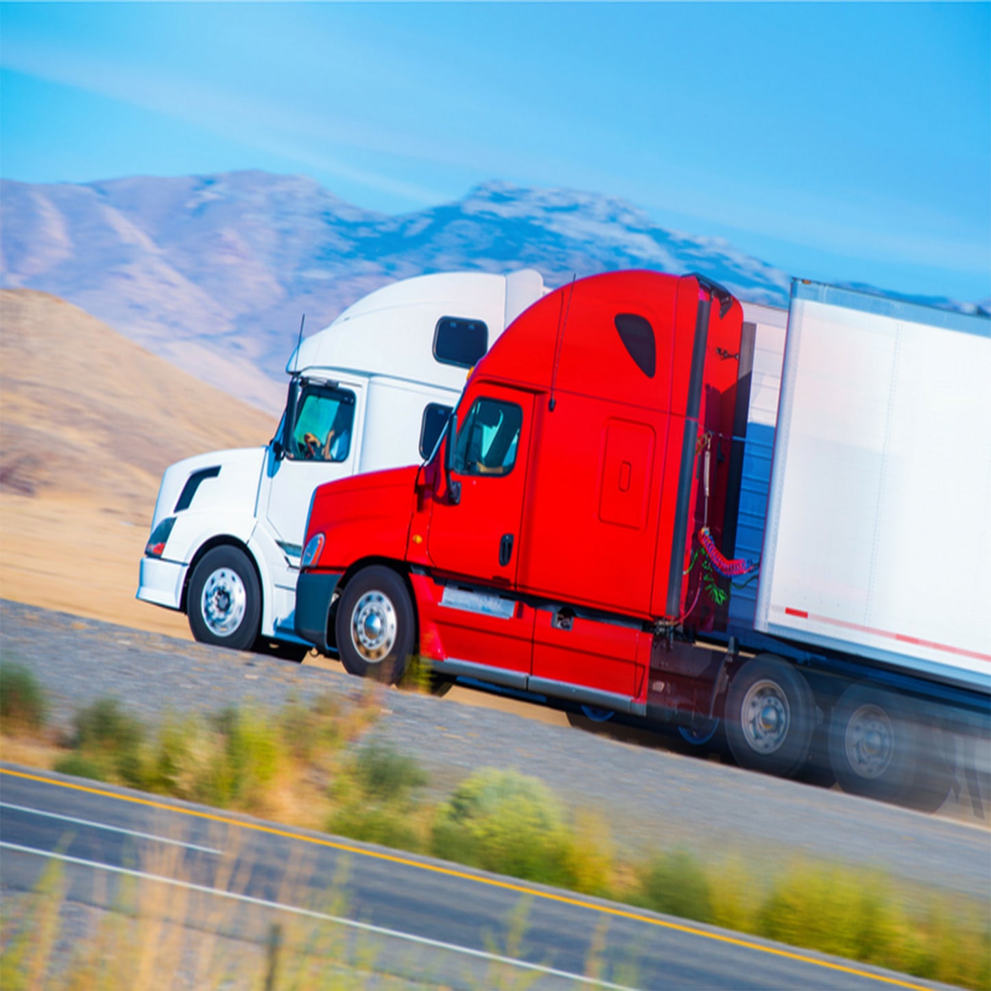 Two trucks, one white and one red, on a road with mountains in the background.
