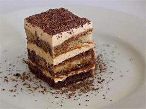 Stacked slice of tiramisu cake with chocolate shavings on a white plate.