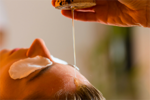 Ayurvedic oil being poured onto a person's forehead during a wellness treatment.