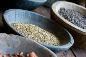Bowls filled with dried Ayurvedic herbs and seeds on a wooden table.