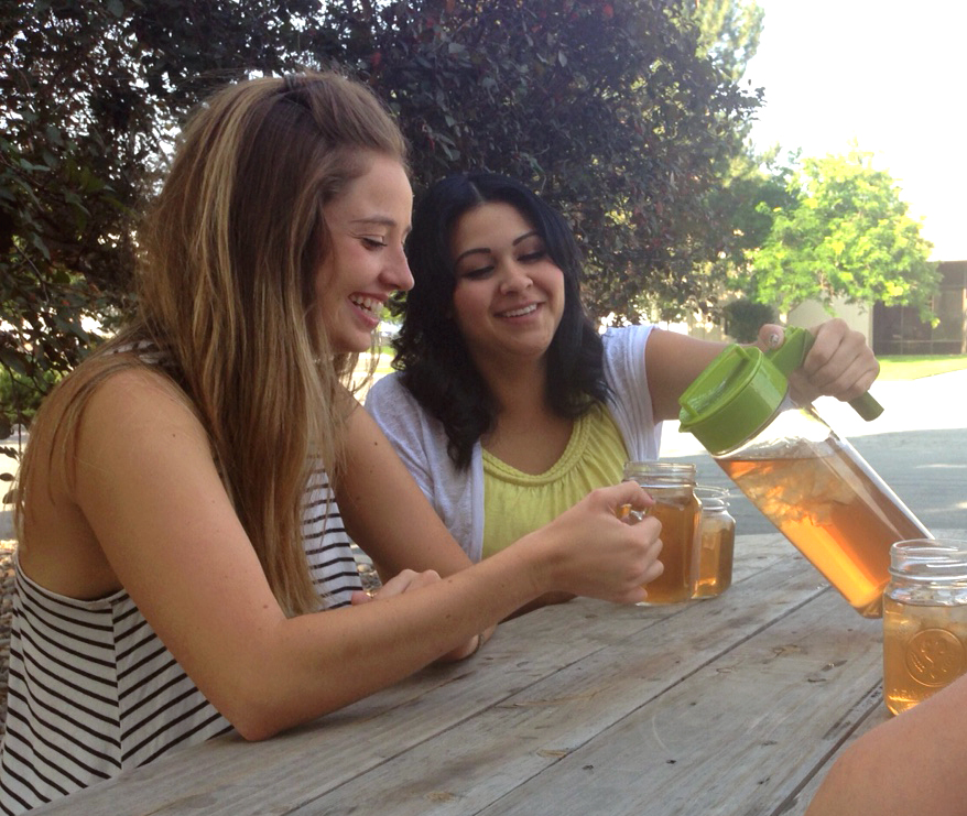 Two women smiling and pouring Davidson's iced tea outdoors.