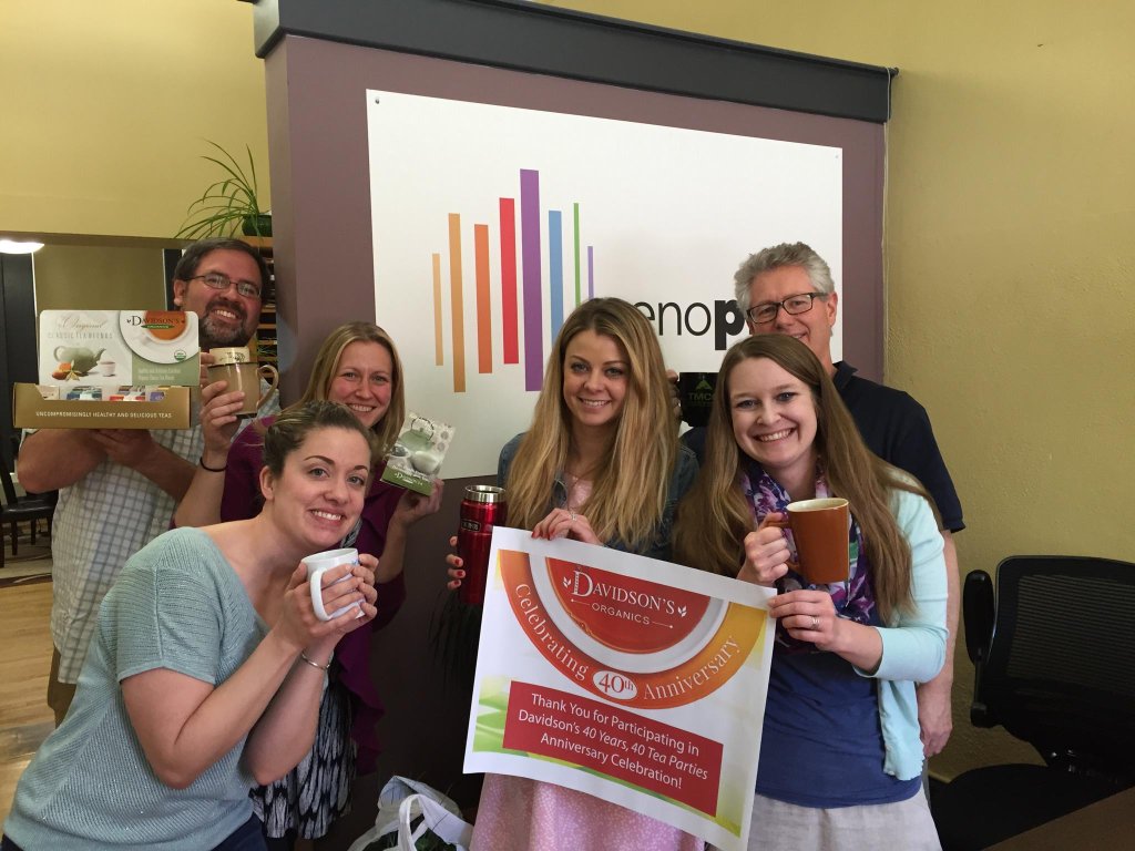 People holding teacups and a Davidson's Tea sign at an event.