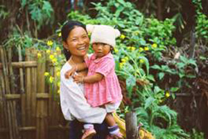 Mother holding her child and smiling in front of a tea farm with flowers.