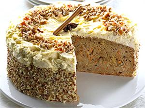 Carrot cake with cream cheese frosting, topped with nuts and a slice removed.