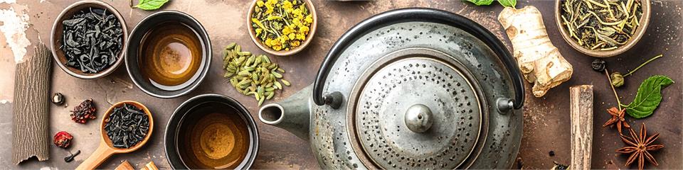 Tea-making setup with teapot, cups, and tea leaves on a wooden surface