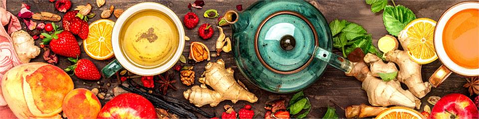 Tea-making setup with tea leaves, fruits, and a teapot on a wooden surface.