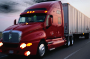 Red semi-truck driving on a road with blurred background.