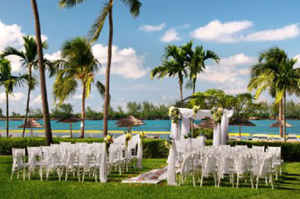Outdoor wedding ceremony set up on grass by a tropical body of water.