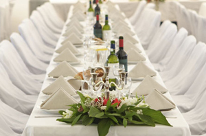 Long white banquet table set with napkins and floral centerpieces.
