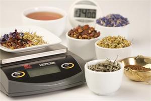 Dried tea leaves and spices on a digital scale, with a timer and cups.